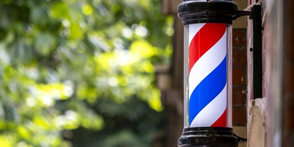 Classic red, white, and blue striped barber pole mounted on an exterior brick wall outside a barbershop